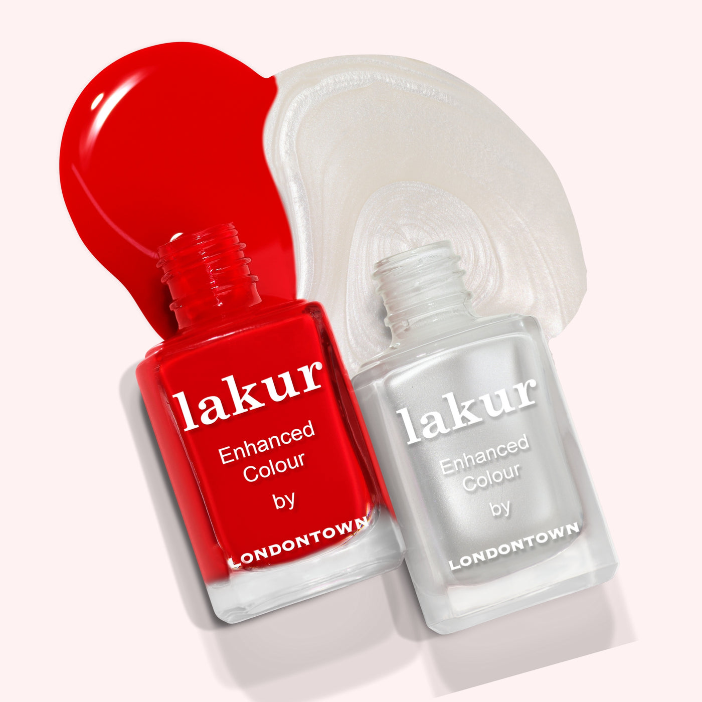 Two bottles of nail polish from the Frosted Berries Duo by LONDONTOWN, one red and one white, create a wintery scene with spilled polish in the background. These "lakur" bottles are perfect for festive nails this season.