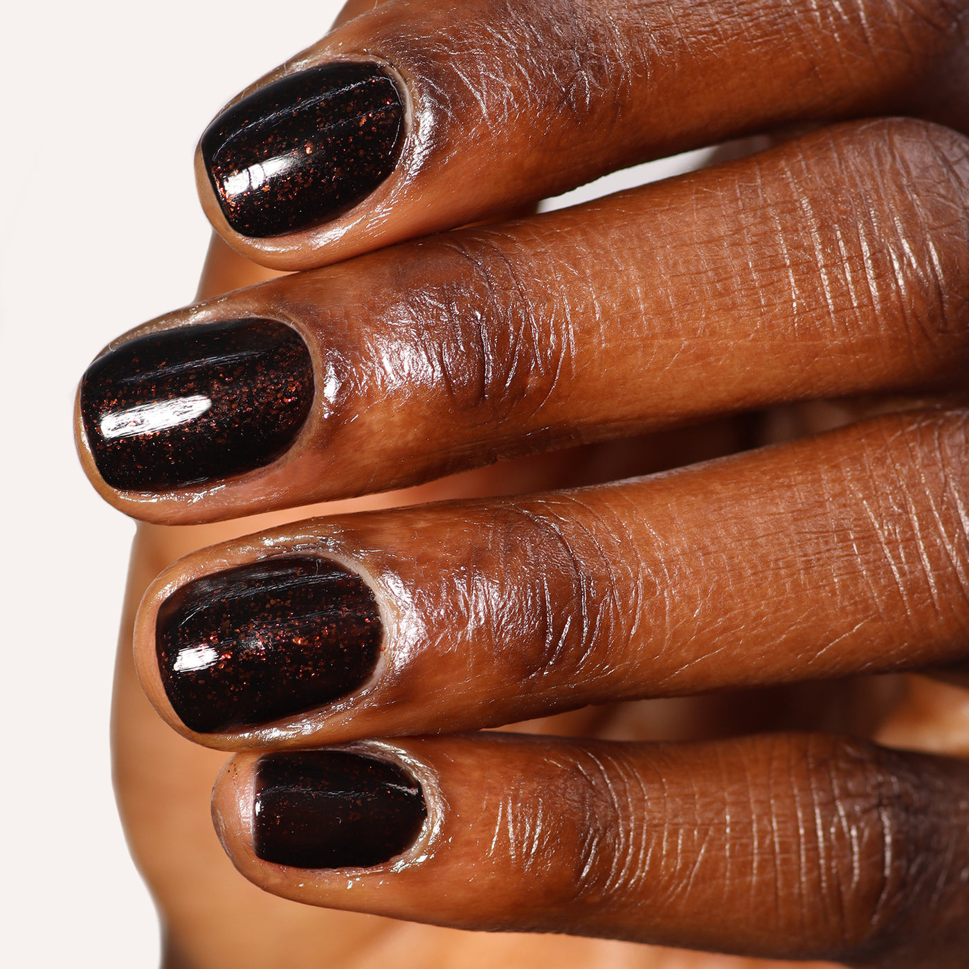 Close-up of a hand with deep, glossy "Around the Fireplace" nail polish by LONDONTOWN on short-trimmed nails, featuring a subtle copper-flecked hue.