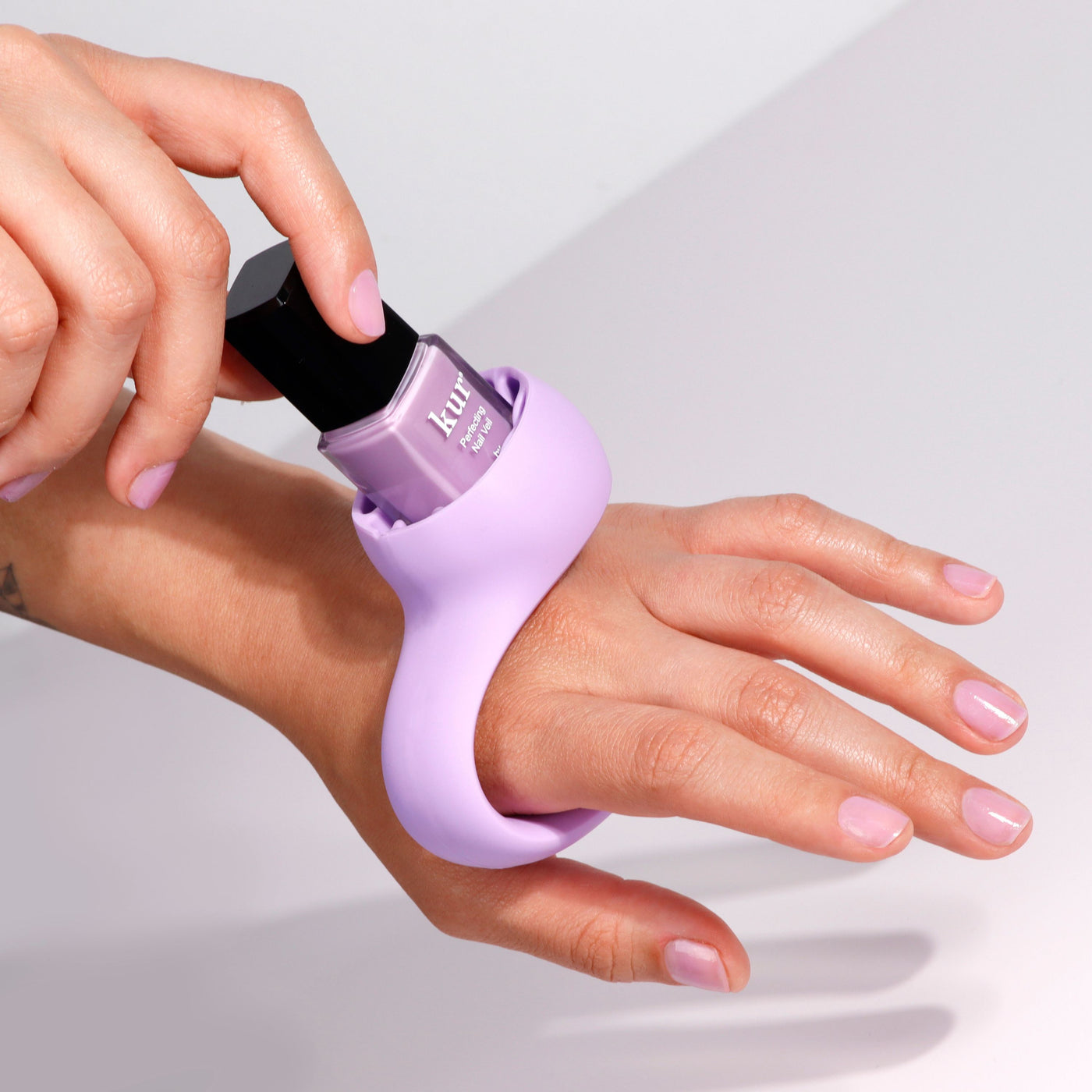 A hand with light purple nail polish is being painted using a nail polish bottle held in the LONDONTOWN Bottle Service Polish Holder - Purple, ensuring an easy, mess-free mani.