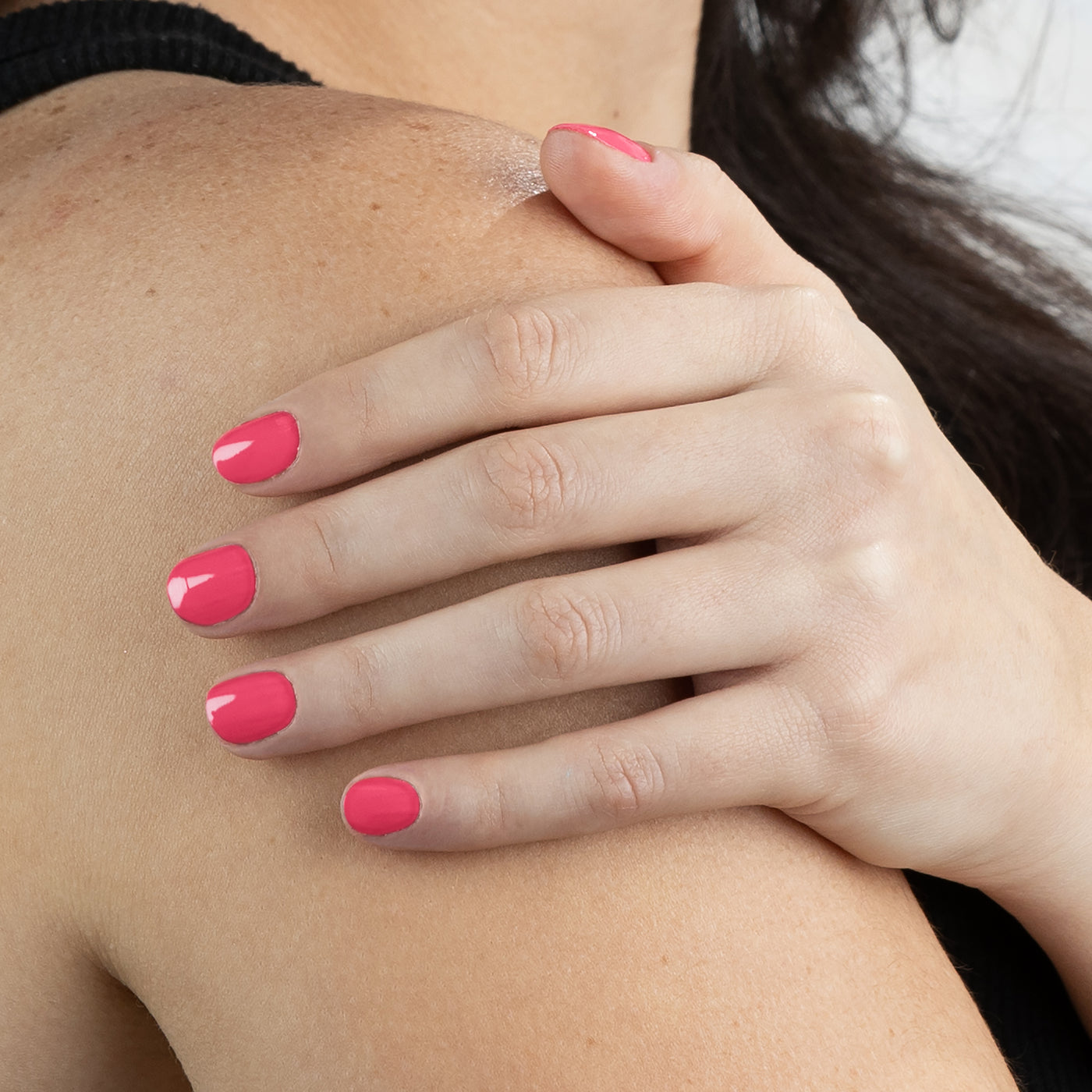 A hand adorned with Electric Flamingo nail polish by LONDONTOWN is resting on a person's shoulder. The person is wearing a black top, and the background is plain.