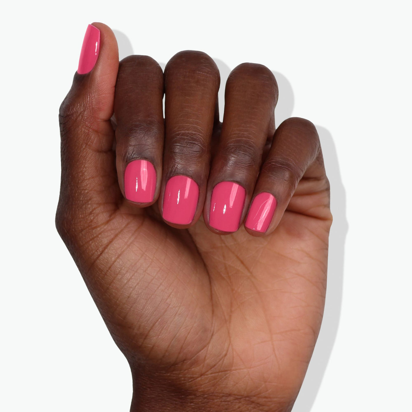 A hand with dark skin showing neatly manicured nails painted in LONDONTOWN's Electric Flamingo, a flamboyant and glossy pink color, against a white background.