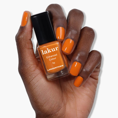 A hand holding a bottle of burnt orange nail polish labeled "Heat Wave (Professional) by LONDONTOWN," with nails painted in the same striking shade.