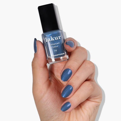 Hand holding a bottle of LONDONTOWN's Blue Diamond (Professional) nail polish in a sporty blue shade, with matching chrome-blue nails.