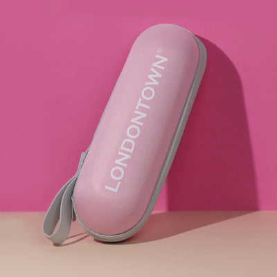 The Signature Mini Umbrella by LONDONTOWN, a stylish pink cylindrical pouch with a grey handle and "LONDONTOWN" printed in white letters on the side, makes for the perfect travel companion, beautifully showcased against a pink and beige background.