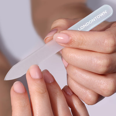 Close-up of a person effortlessly filing their nails with the "Glass Nail File - Milky" from LONDONTOWN. The nails, adorned with light pink polish, enjoy damage-free perfection.