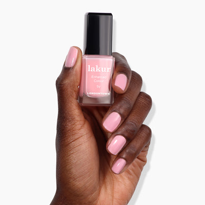 A hand with manicured nails holds a bottle of "Perfecting Nail Veil #7 (Professional)" by LONDONTOWN in a light pink shade, showcasing the power-packed care and vibrant color it provides.