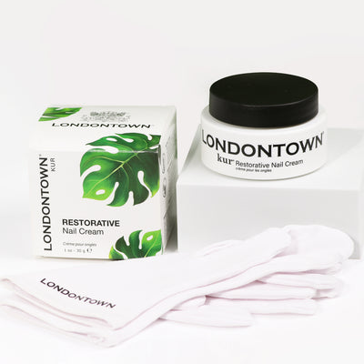 LONDONTOWN's Restorative Nail Cream, showcased with its box, jar, and a pair of white gloves on a white surface, serves as an excellent transformative moisturizer for dry nails.