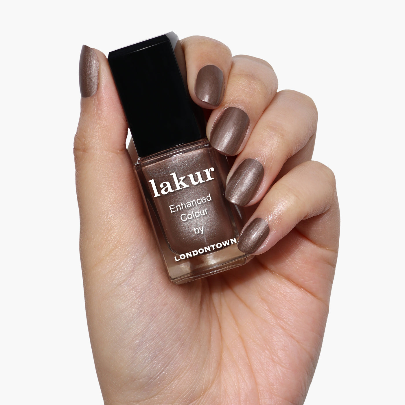 A hand with neatly manicured nails painted in antique bronze holds a bottle of LONDONTOWN Lakur nail polish in the shade Nightcap.