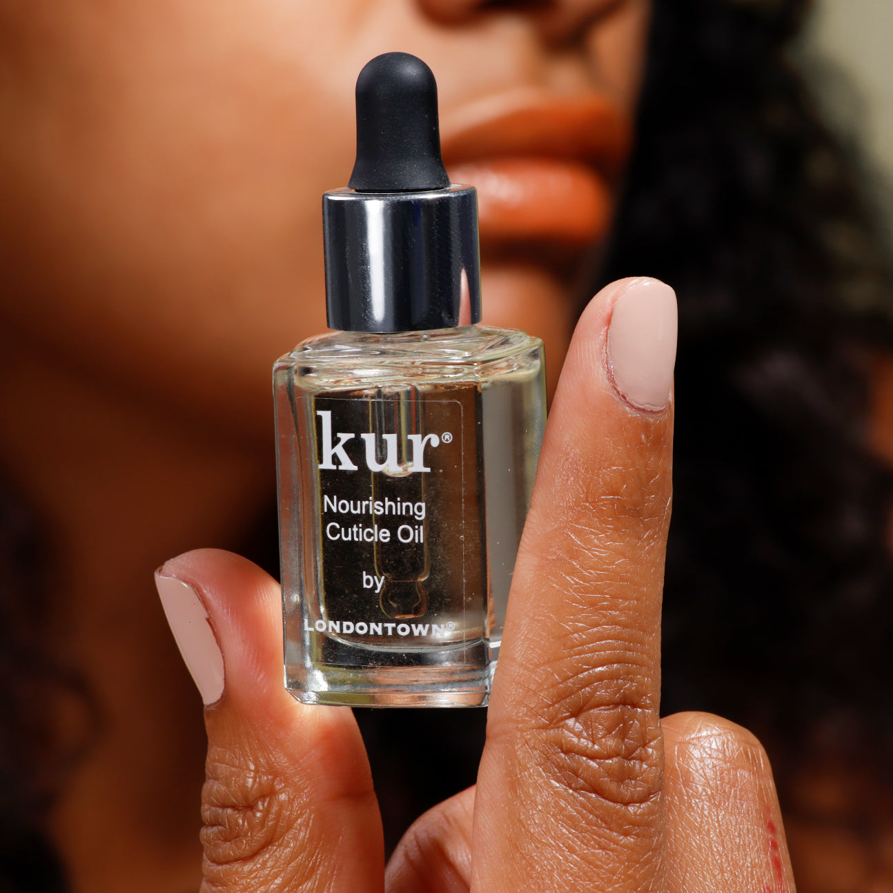 A person holds a bottle of LONDONTOWN's Nourishing Cuticle Oil with a dropper, enriched with the Florium Complex. Their nails, painted light pink, bask in the promise of nail restoration.