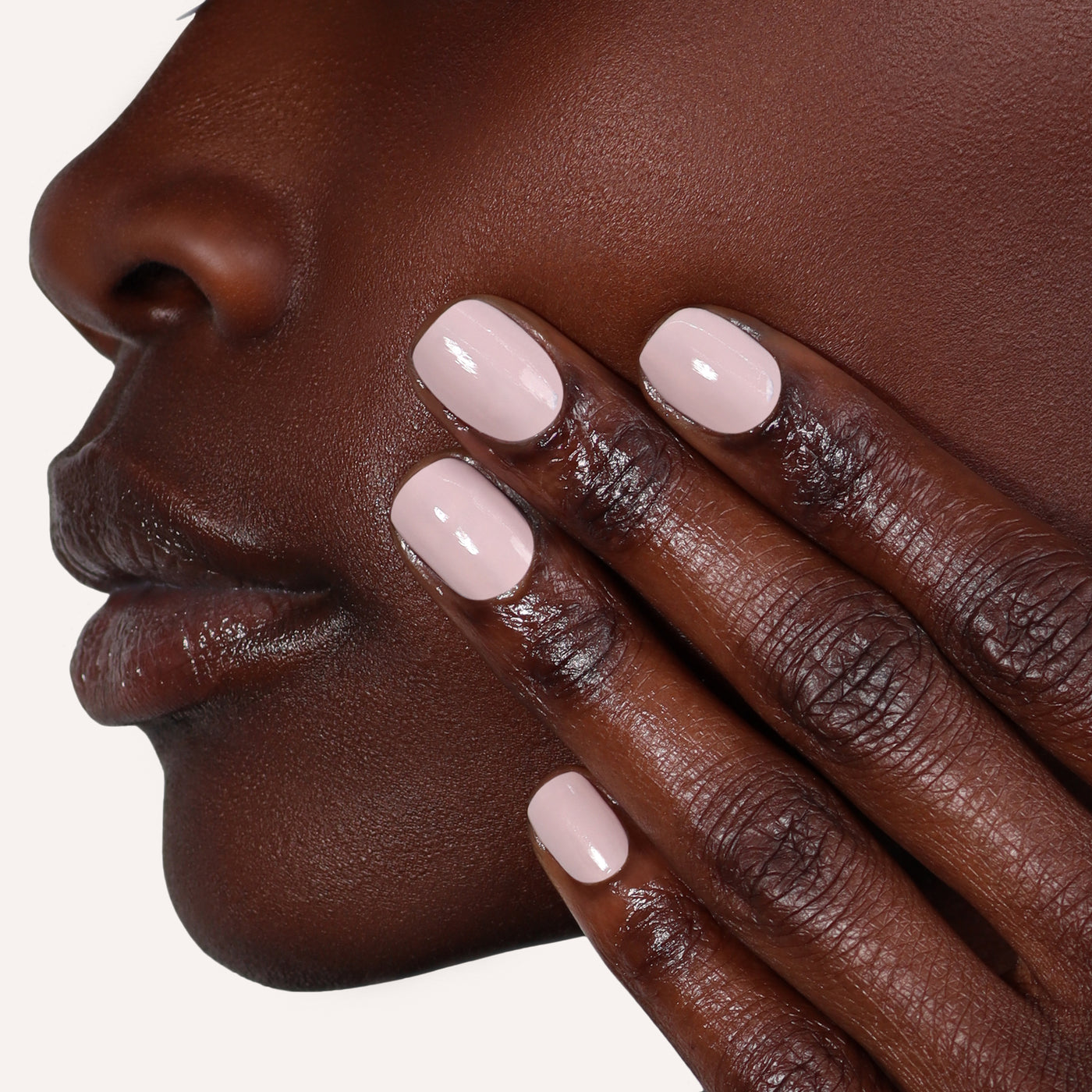 Close-up of a person's face and hand with manicured nails. The skin is smooth and dark, and the nails are polished in LONDONTOWN's Off the Record, a cool mauve color. The hand is gently touching the face near the jawline.