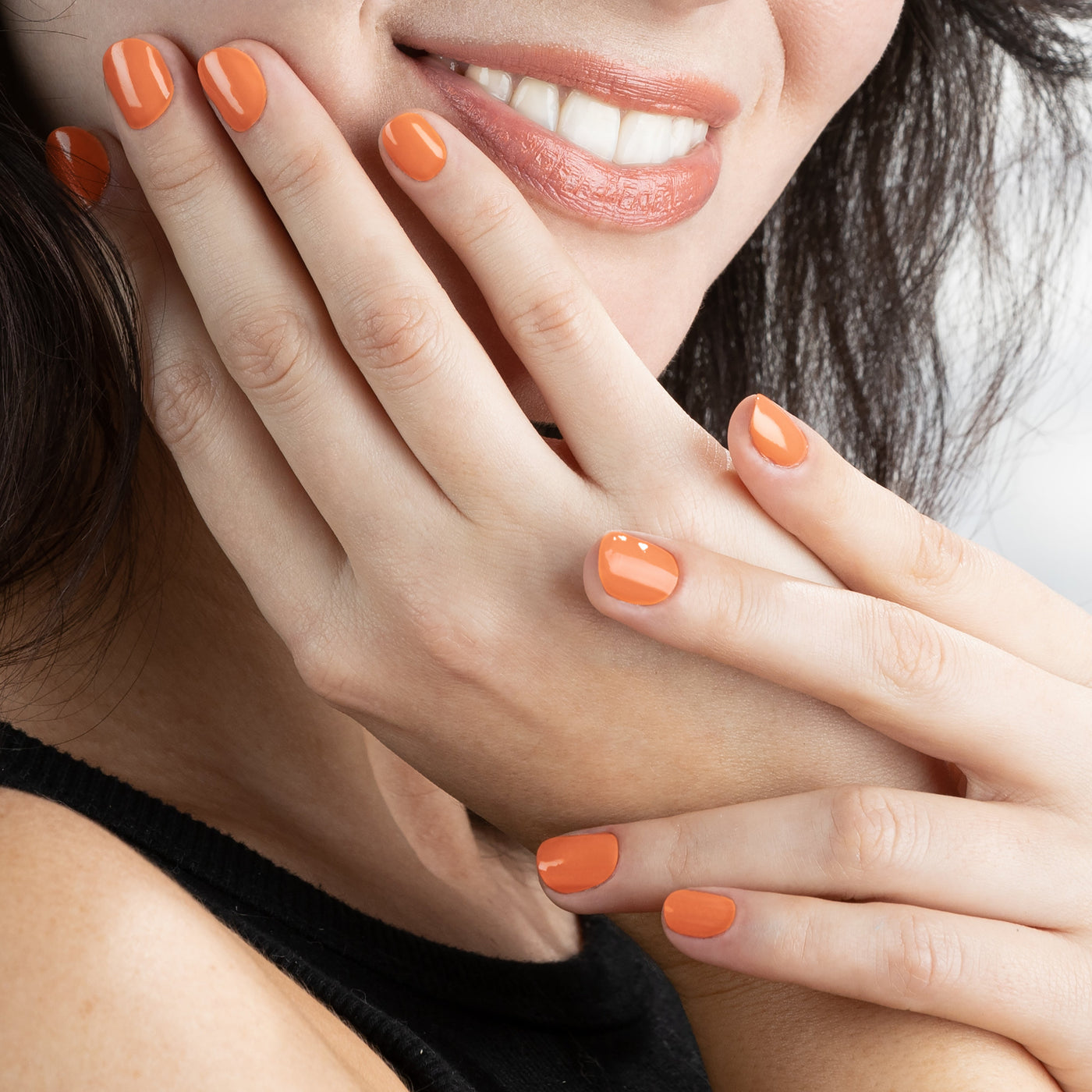 A woman with "Paloma" by LONDONTOWN on her nails smiles, showcasing her manicured hands close to her face, reminiscent of a California peach.