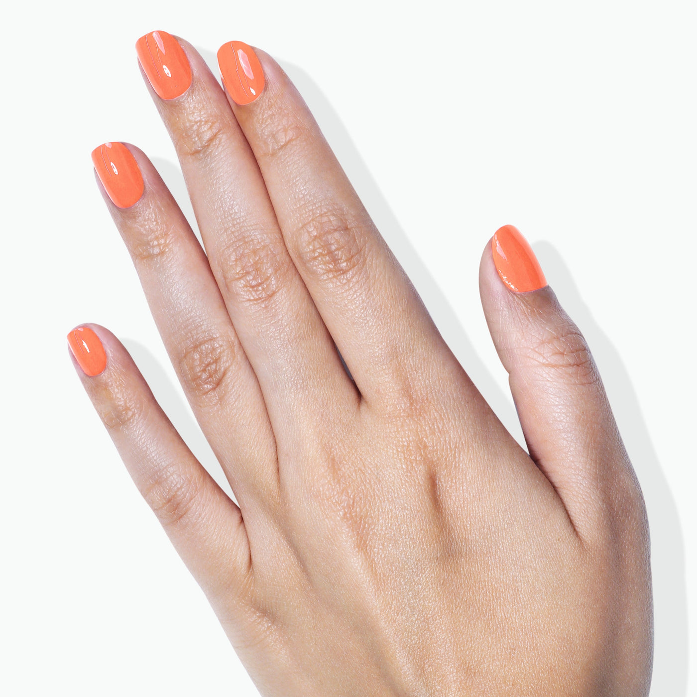 A hand with neatly manicured fingernails painted in the vibrant, bright orange 'Paloma' polish from LONDONTOWN against a light background.