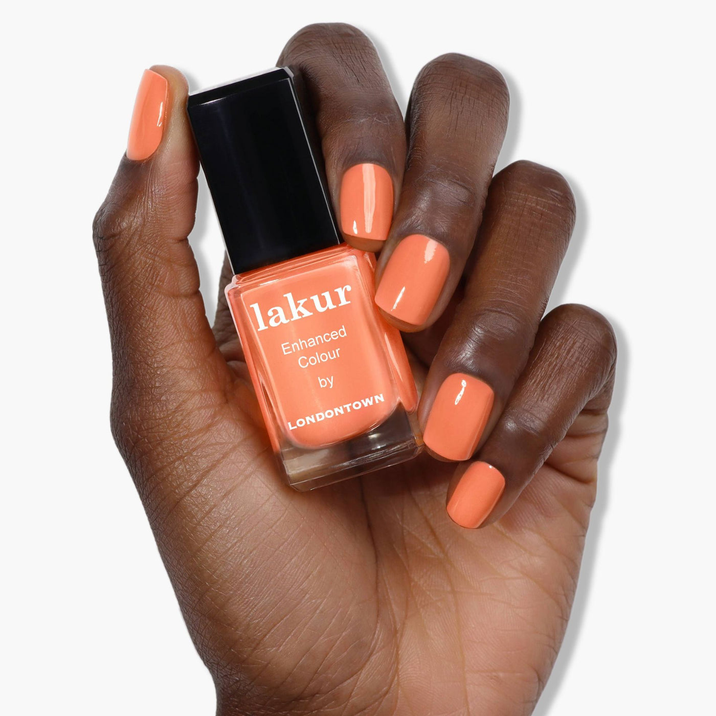 A hand with orange nail polish, resembling a vibrant peach, holds a matching bottle of Paloma by LONDONTOWN.