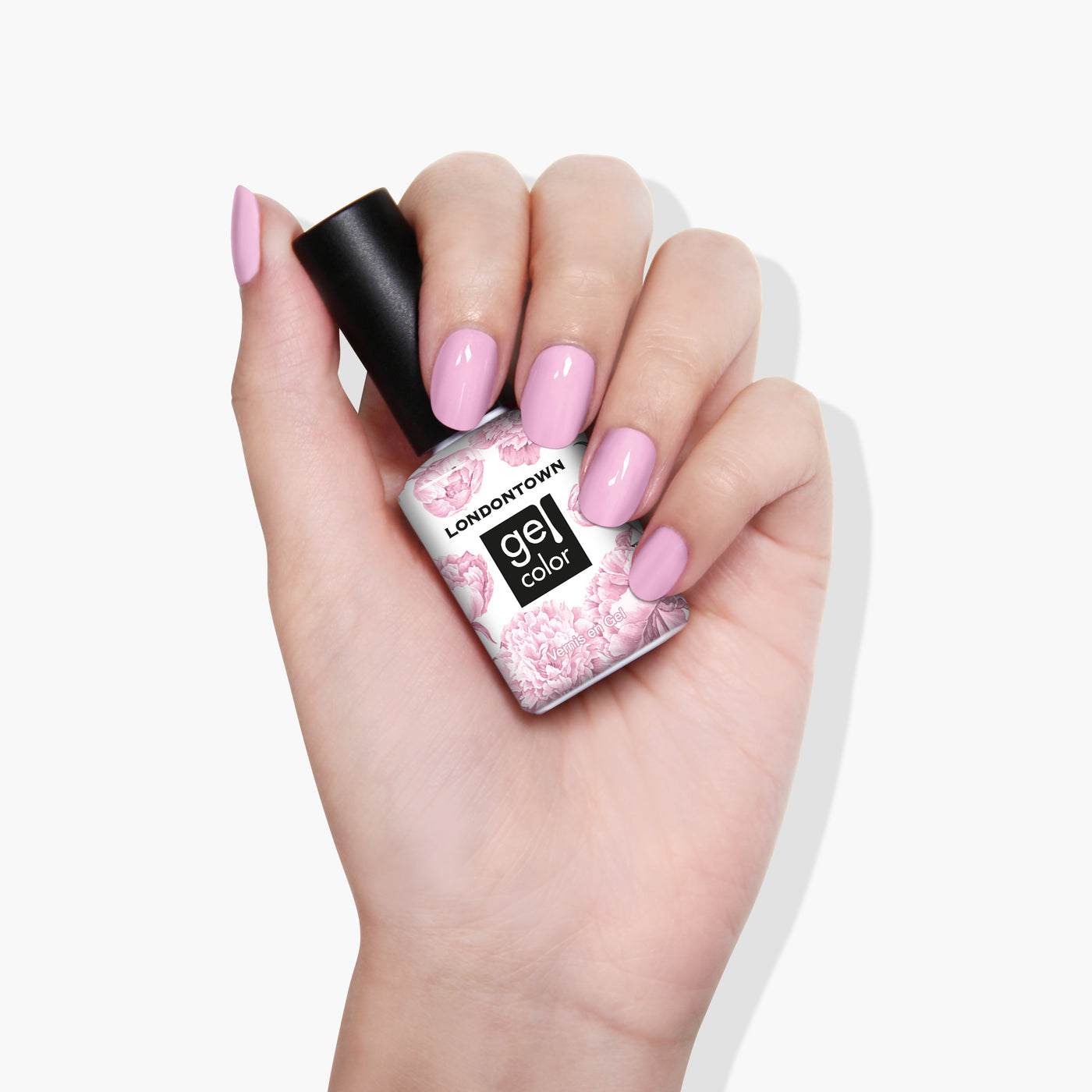 A hand with manicured nails painted a pastel shade of light pink holds a bottle of LONDONTOWN's "Pink Palm" gel color nail polish, adorned with a floral design resembling delicate carnations.