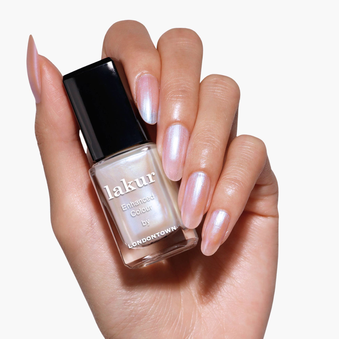 A hand with a pale pink iridescent manicure holds a bottle of LONDONTOWN Pixi Chrome nail polish with a black cap, showcasing its stunning crème-to-chrome finish.