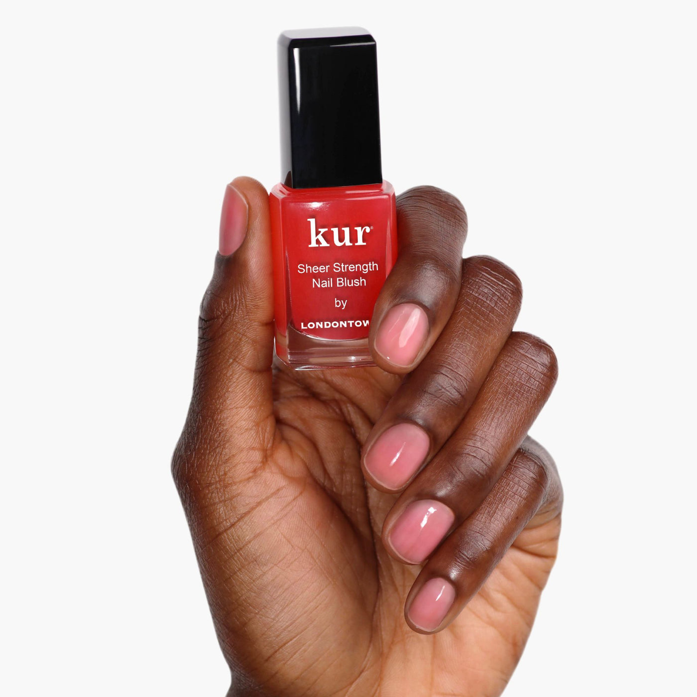 A hand holds a bottle of LONDONTOWN Sheer Strength Nail Blush - Poppy in bright red. Fingernails are polished with a pink shade, radiating a healthy glow boosted by this nail hardener.