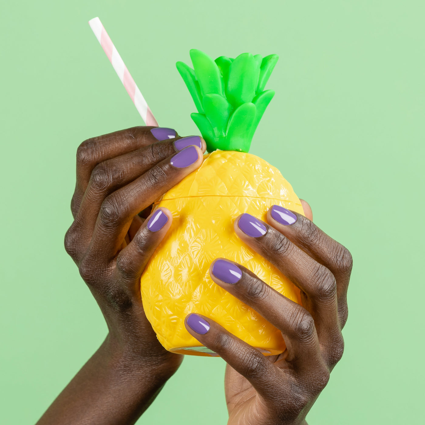 The psychedelic green background frames a pineapple-shaped cup with a pink and white striped straw, held by two hands adorned with "Road Trip" lavender nail polish from LONDONTOWN.