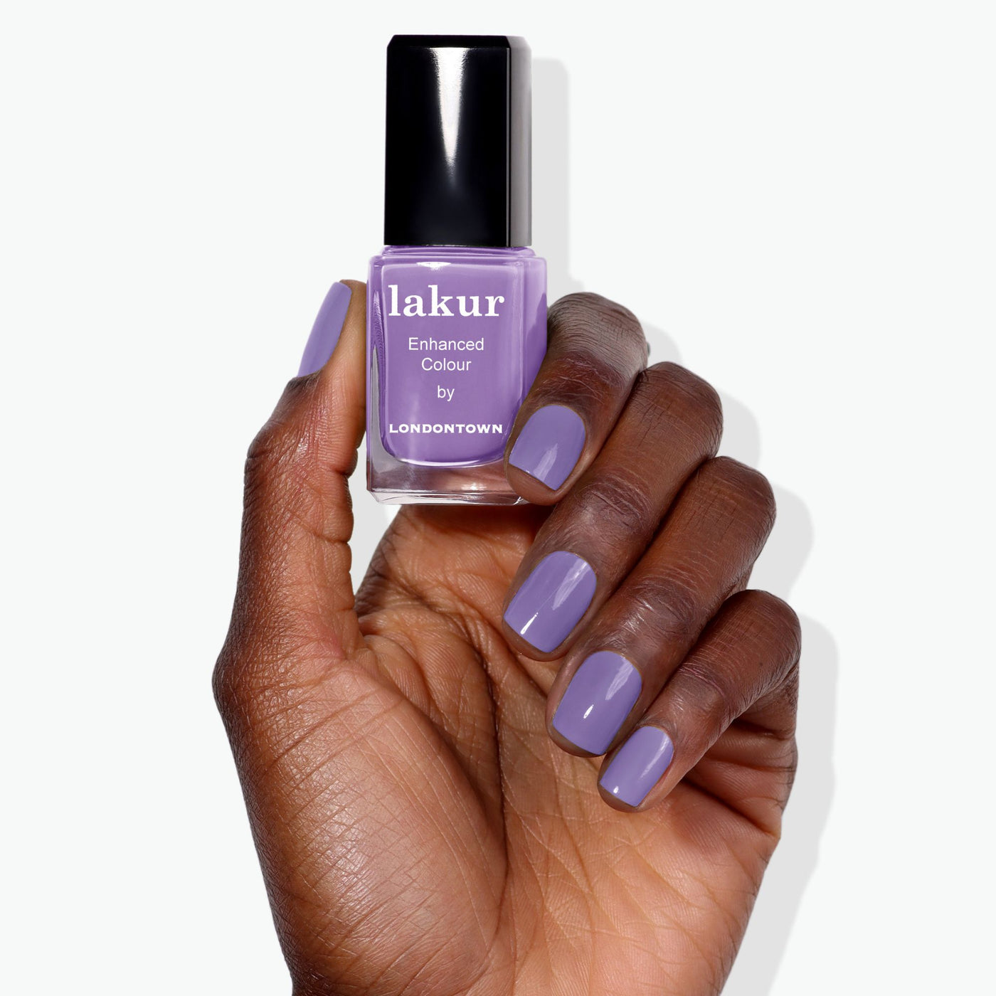 A hand with manicured nails painted in a psychedelic lavender holds a bottle of LONDONTOWN Road Trip Enhanced Colour nail polish in a matching shade.