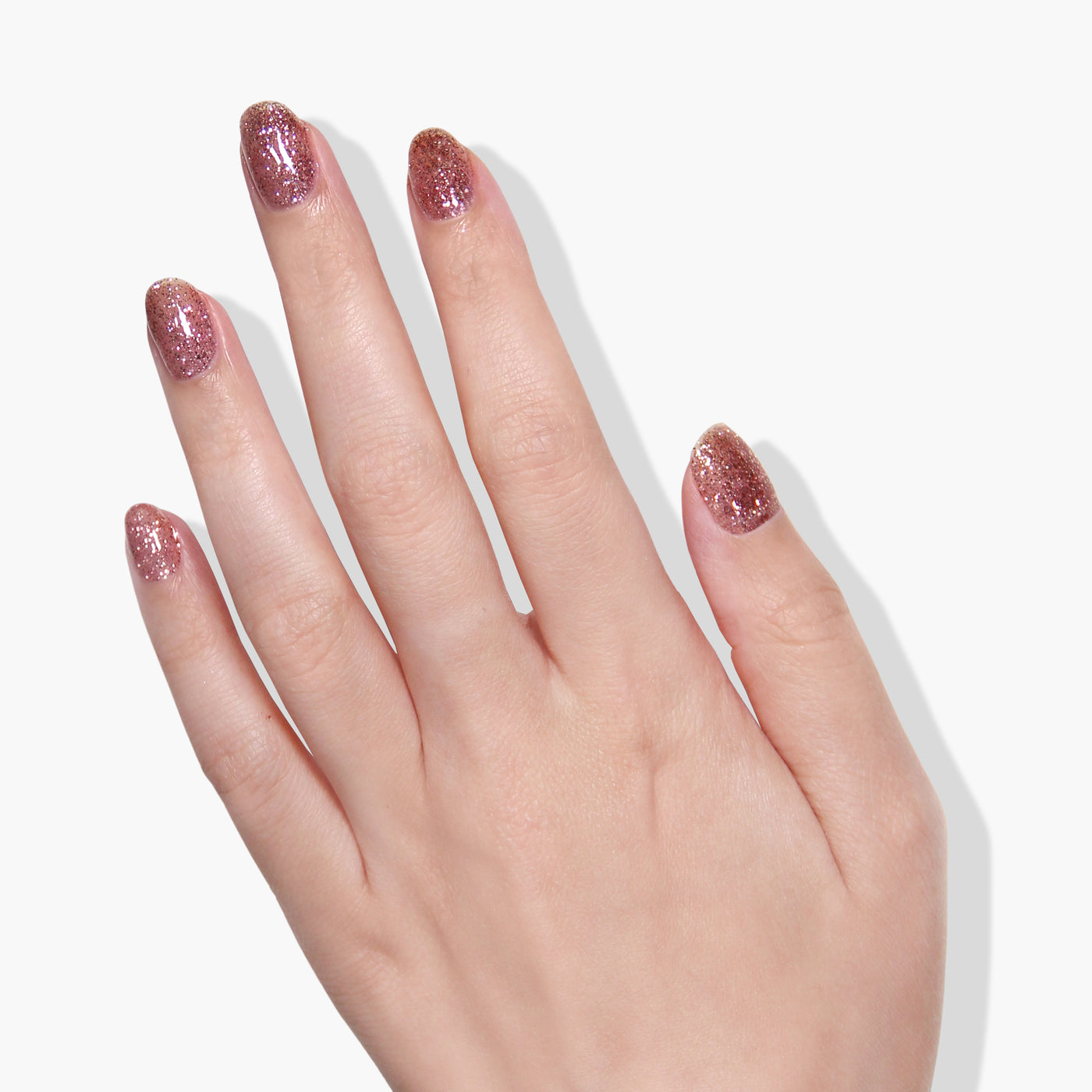 A hand adorned with LONDONTOWN's Rosé All Day glittery pink nail polish on all fingers against a white background.