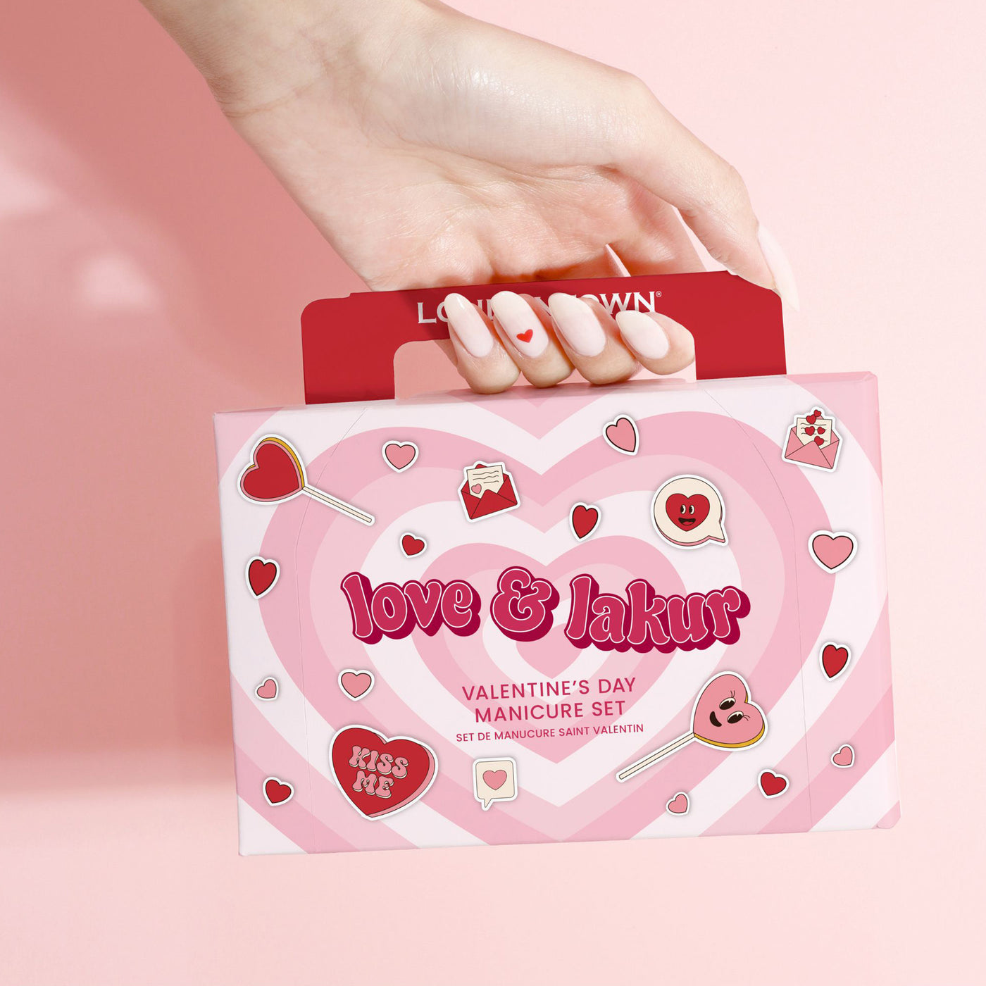 A hand holds a limited-edition LONDONTOWN Love & lakur Valentine’s Day Set with heart-themed pink and red packaging, against a pink background.