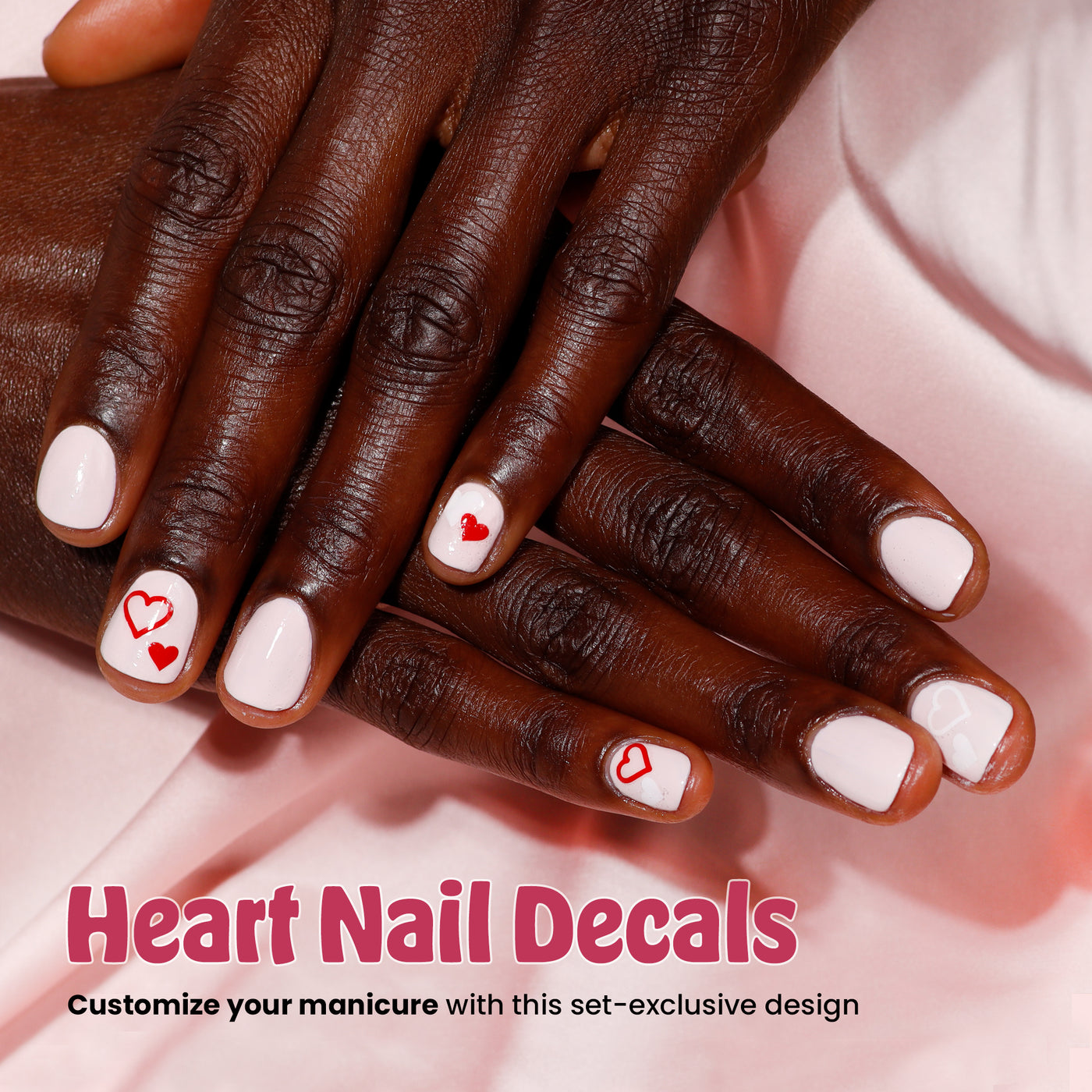 Hands adorned with pink nail polish and red heart decals resting on a pink fabric backdrop. Text reads: "Love & lakur Valentine’s Day Set by LONDONTOWN - Personalize your limited-edition manicure with this exclusive design.