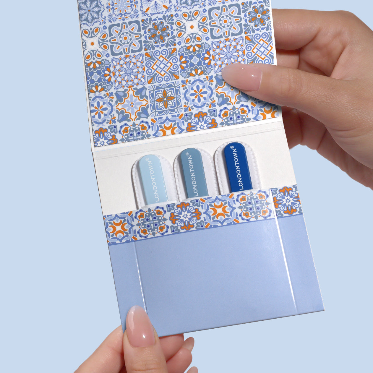 Hands holding the LONDONTOWN Mini Nail File Set, neatly filed and ready to go, featuring three colorful nail files in a decorative folder with a blue and orange geometric pattern on the cover.