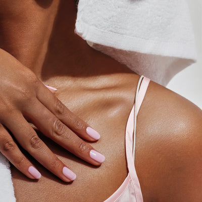 Close-up of a person's shoulder draped with a white towel, highlighting LONDONTOWN's versatile Magnolia Haze nail polish that perfectly complements their sheer light pink strap top.