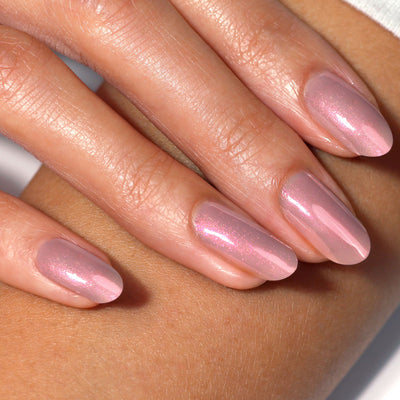 Close-up of a hand with long, almond-shaped nails painted in shimmery pastel pink LONDONTOWN Aurora Chrome lakur polish.