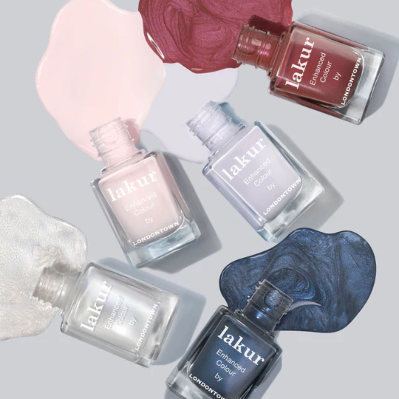 Five bottles of LONDONTOWN's Ski Bunny lakur nail polish in assorted colors, featuring a delicate pink-tinted cream, are arranged with matching spilled swatches on a light background.