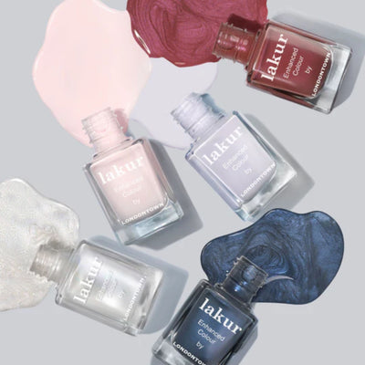 Five bottles of LONDONTOWN's Ski Bunny lakur nail polish in assorted colors, featuring a delicate pink-tinted cream, are arranged with matching spilled swatches on a light background.