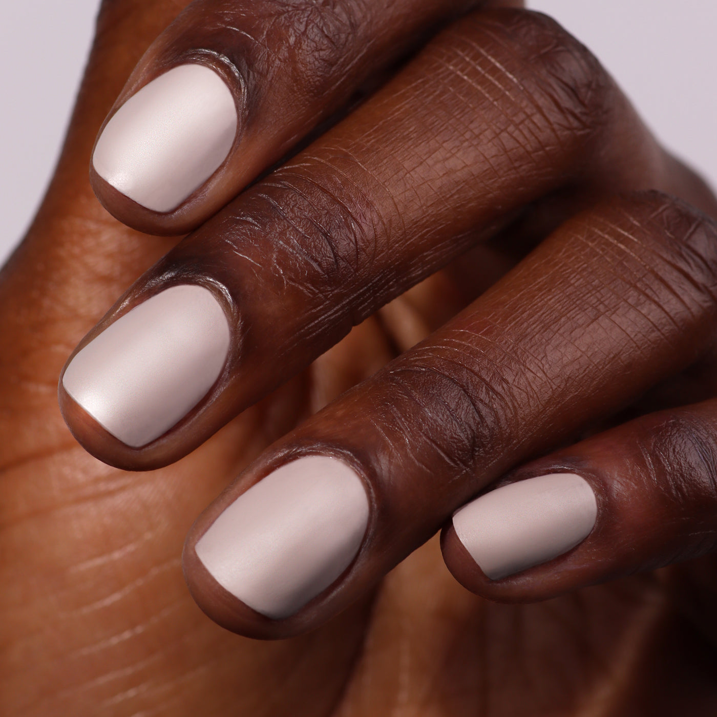 A close-up of a hand with neat nails displays an ultra-luxe suede-like finish, featuring LONDONTOWN's pale matte color using the Matte Top Coat (Professional), set against a plain background.