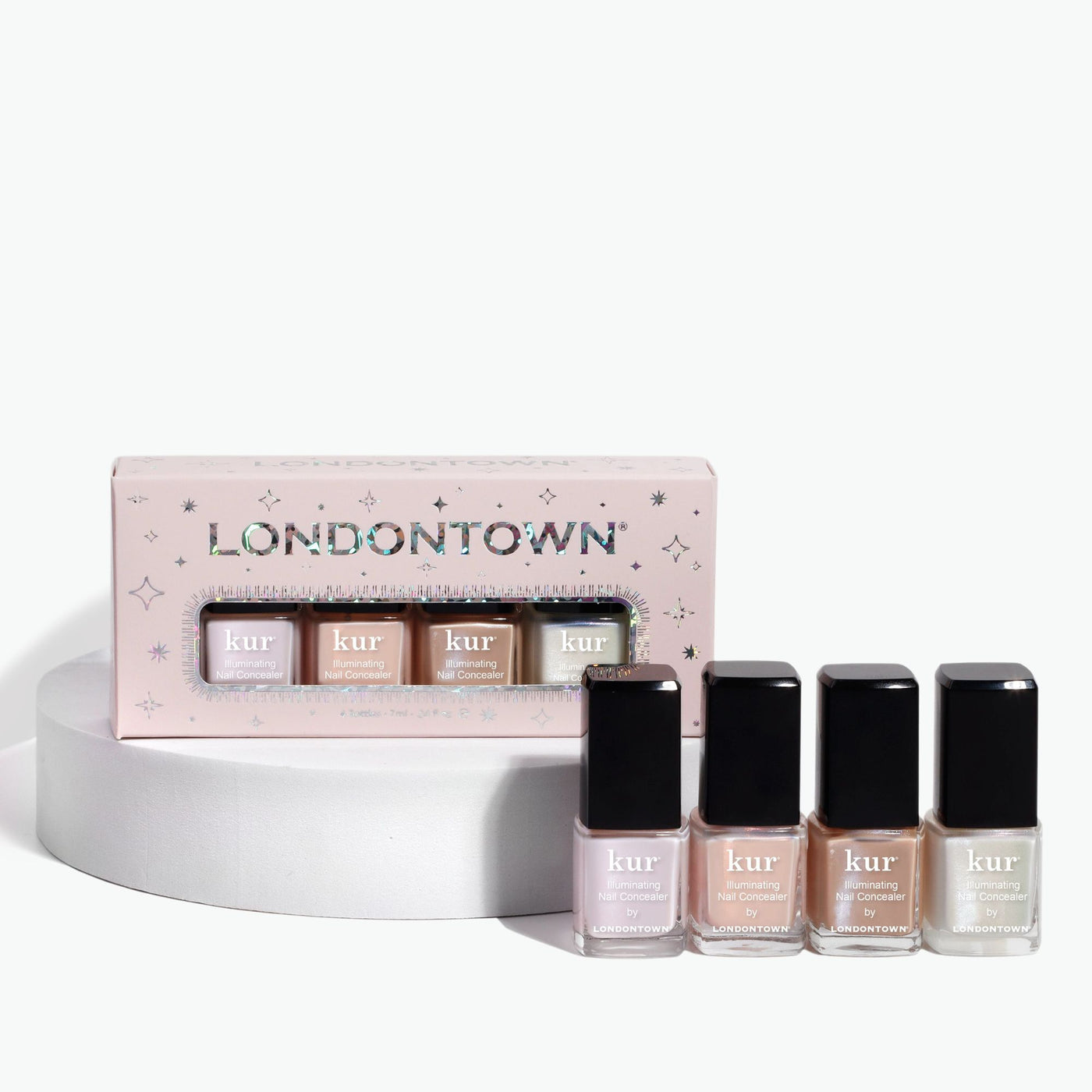 Four bottles of LONDONTOWN nail polish, featuring an exclusive shade, are displayed in front of a beautifully packaged Illuminating Essentials Mini Concealer Set.