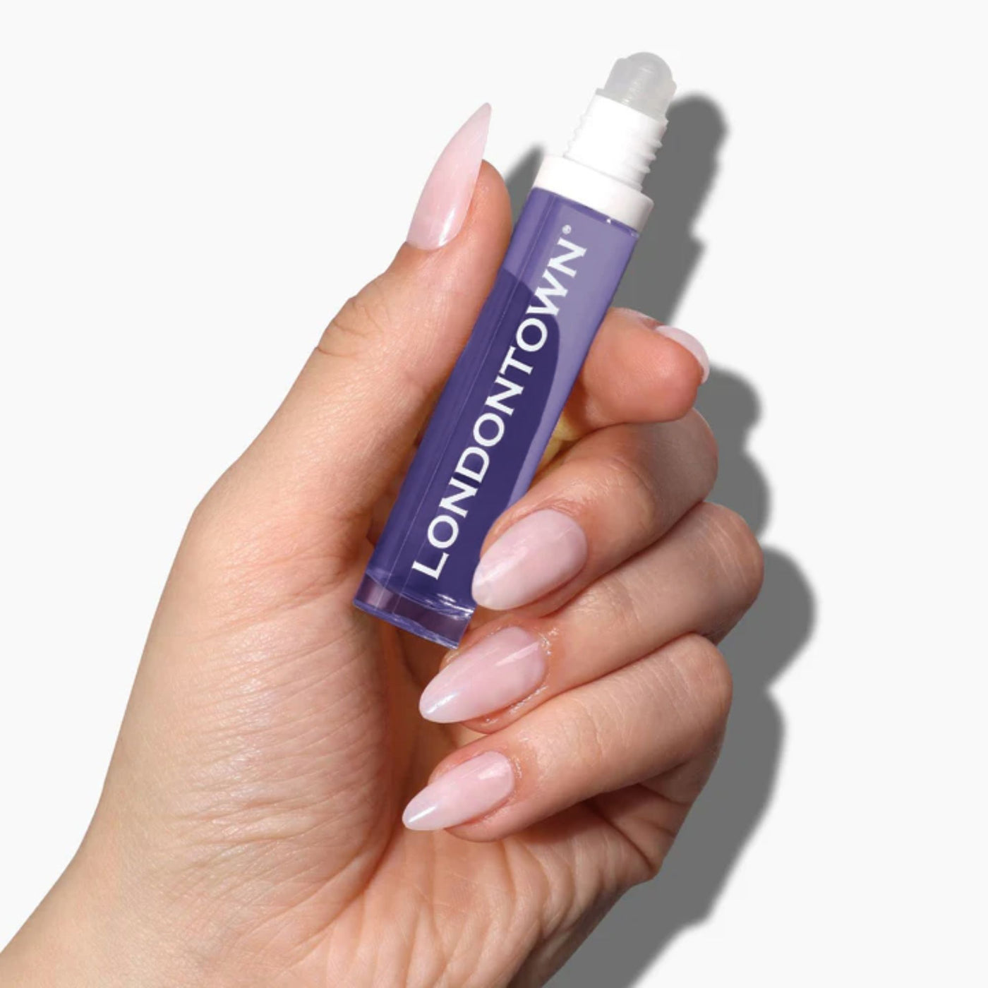 A hand holds the pocket-sized, purple tube of LONDONTOWN Roll & Glow Cuticle Oil - Passion Fruit against a white background.