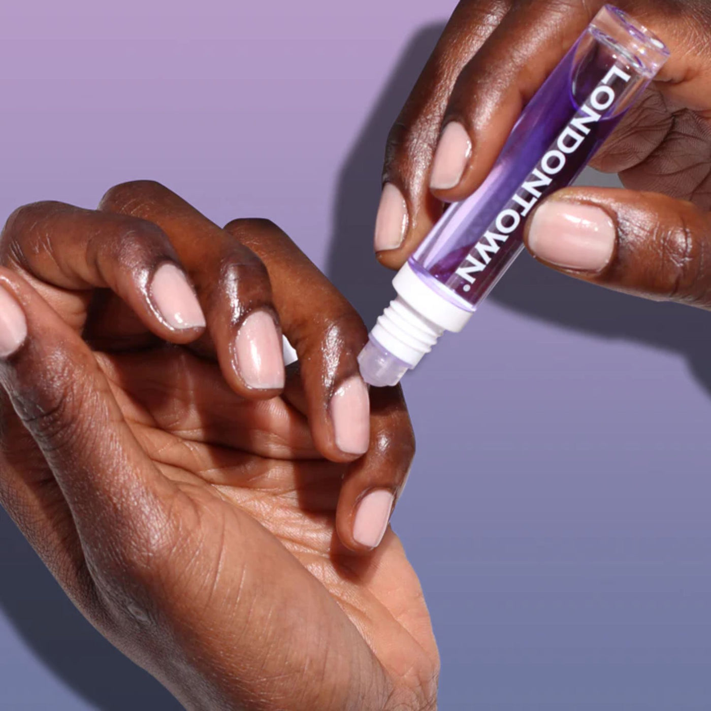 A person is applying the Roll & Glow Cuticle Oil - Passion Fruit from a pocket-sized tube labeled "LONDONTOWN" onto their fingernails.