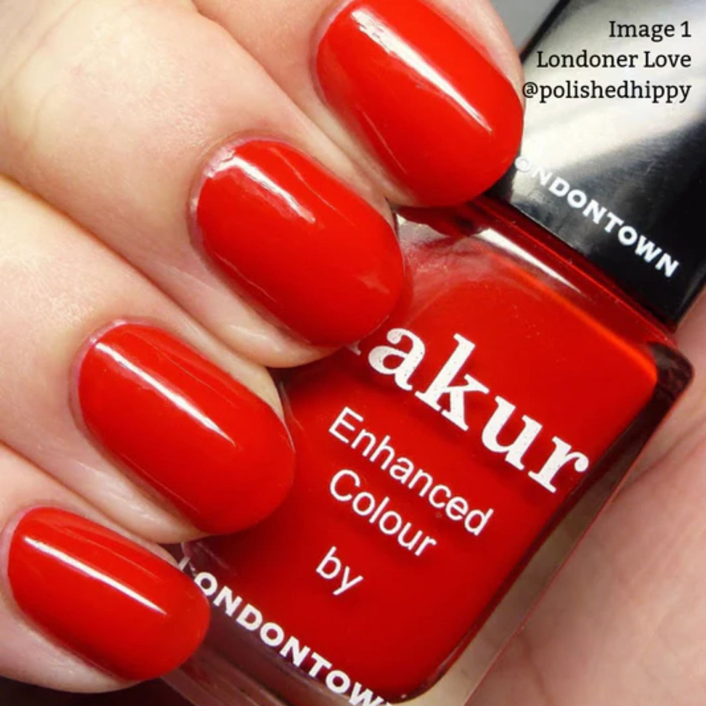 A hand with neatly manicured nails painted in vibrant red crème polish holds a bottle of LONDONTOWN's vegan, cruelty-free "Londoner Love" (Professional) nail lacquer.