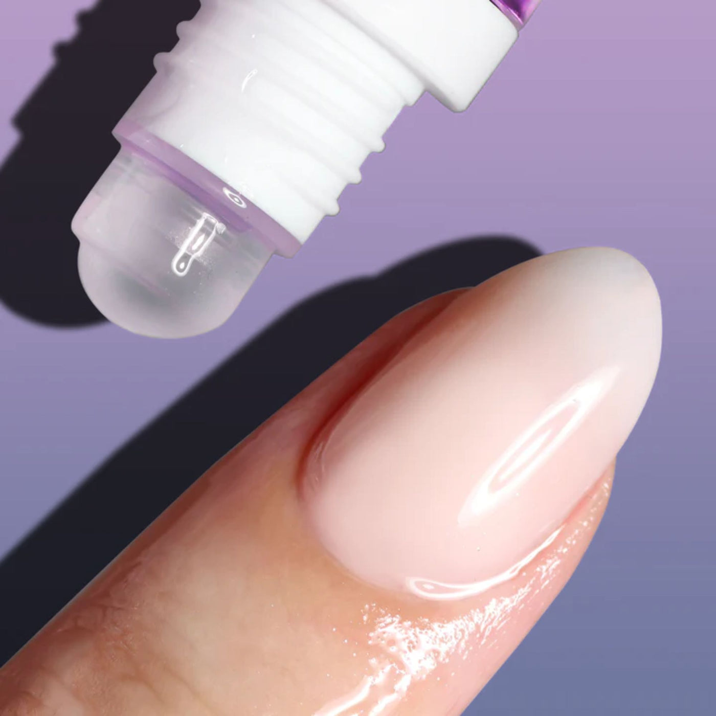 A pocket-sized roll-on applicator dispenses clear LONDONTOWN Roll & Glow Cuticle Oil - Passion Fruit onto a fingertip against a purple background.