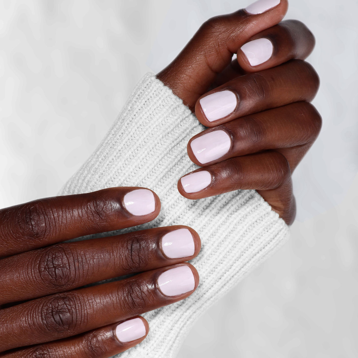 Hands with neatly manicured nails in LONDONTOWN's Ski Bunny, a light pink cream shade, emerge gracefully from the soft confines of a white knit sweater sleeve.