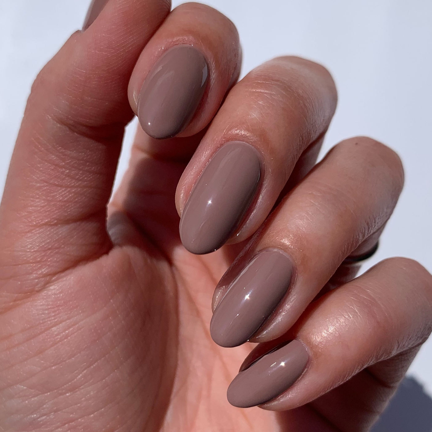 A hand with neatly manicured nails flaunts a glossy taupe color enhanced by LONDONTOWN's Flash Dry Top Coat, guaranteeing a smooth finish. The fast-dry formula ensures your look is ready in a flash.