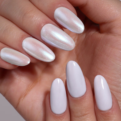 A hand with manicured nails shines in glossy white and iridescent Moonstone Chrome by LONDONTOWN. Almond-shaped nails dazzle with a crème-to-chrome effect, capturing light magnificently.