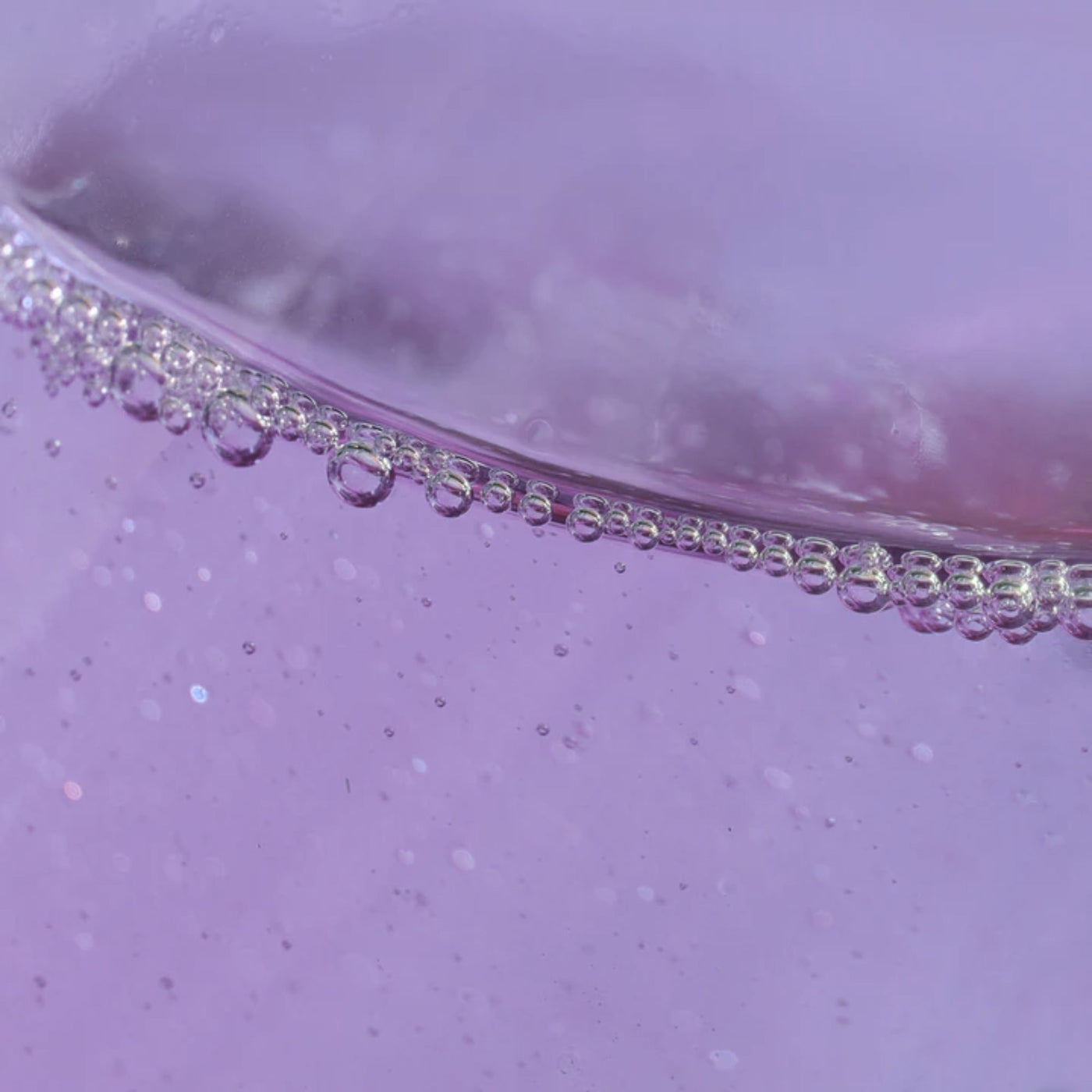 Close-up of a purple liquid surface with small bubbles lining the edge, reminiscent of the sparkling appearance of LONDONTOWN's Roll & Glow Cuticle Oil - Passion Fruit.