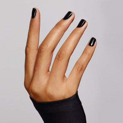 A hand with LONDONTOWN's Matte Top Coat (Professional) black polish, featuring a suede-like finish, fingers spread elegantly on a contrasting plain background and accented by an ultra-luxe black sleeve.