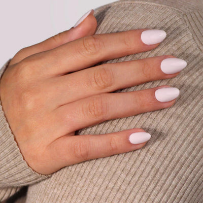 A hand with nails polished in LONDONTOWN's Ski Bunny (Professional) light pink shade rests gently on a beige ribbed fabric, evoking the soft, soothing grace of pink-tinted cream.