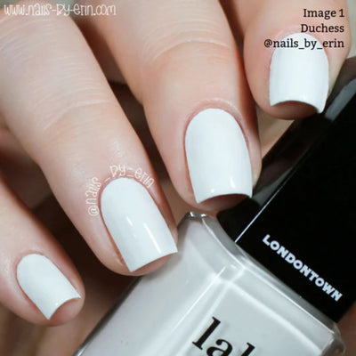 A hand displays nails painted in "Duchess," a crème white polish by LONDONTOWN, evoking a chic French manicure. This vegan, cruelty-free product ensures style and conscience are impeccable.