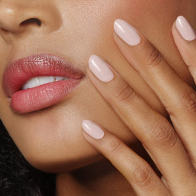 A close-up of a person with glossy pink lips and light pink, almond-shaped nails touched their cheek, exuding a dazzle them all allure with LONDONTOWN's Invisible Crown (Professional).