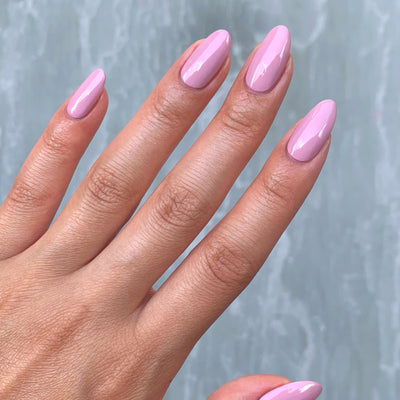 Long, almond-shaped nails flaunt a glossy pink hue using LONDONTOWN's Flash Dry Top Coat, set against a gray backdrop.