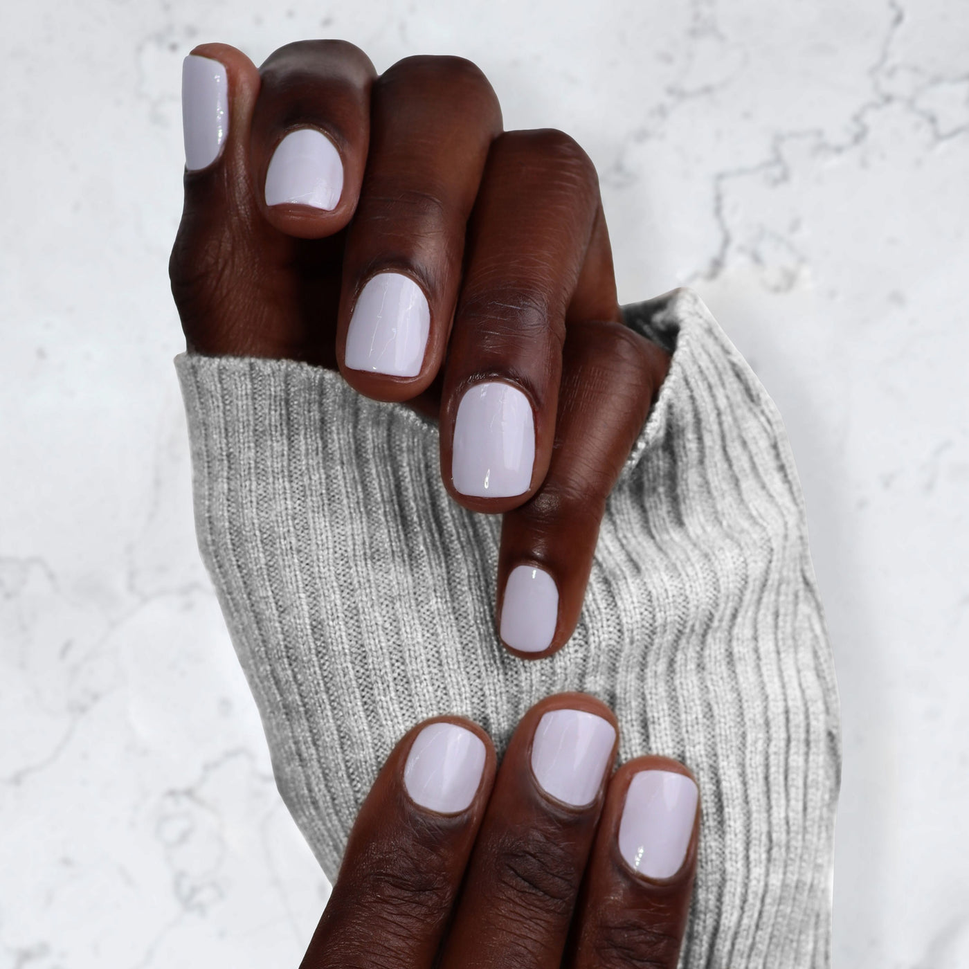 A person with dark skin displays freshly manicured hands in light gray polish resembling a gel mani, enhanced by LONDONTOWN's Gel Genius Top Coat, while wearing a gray ribbed sweater.