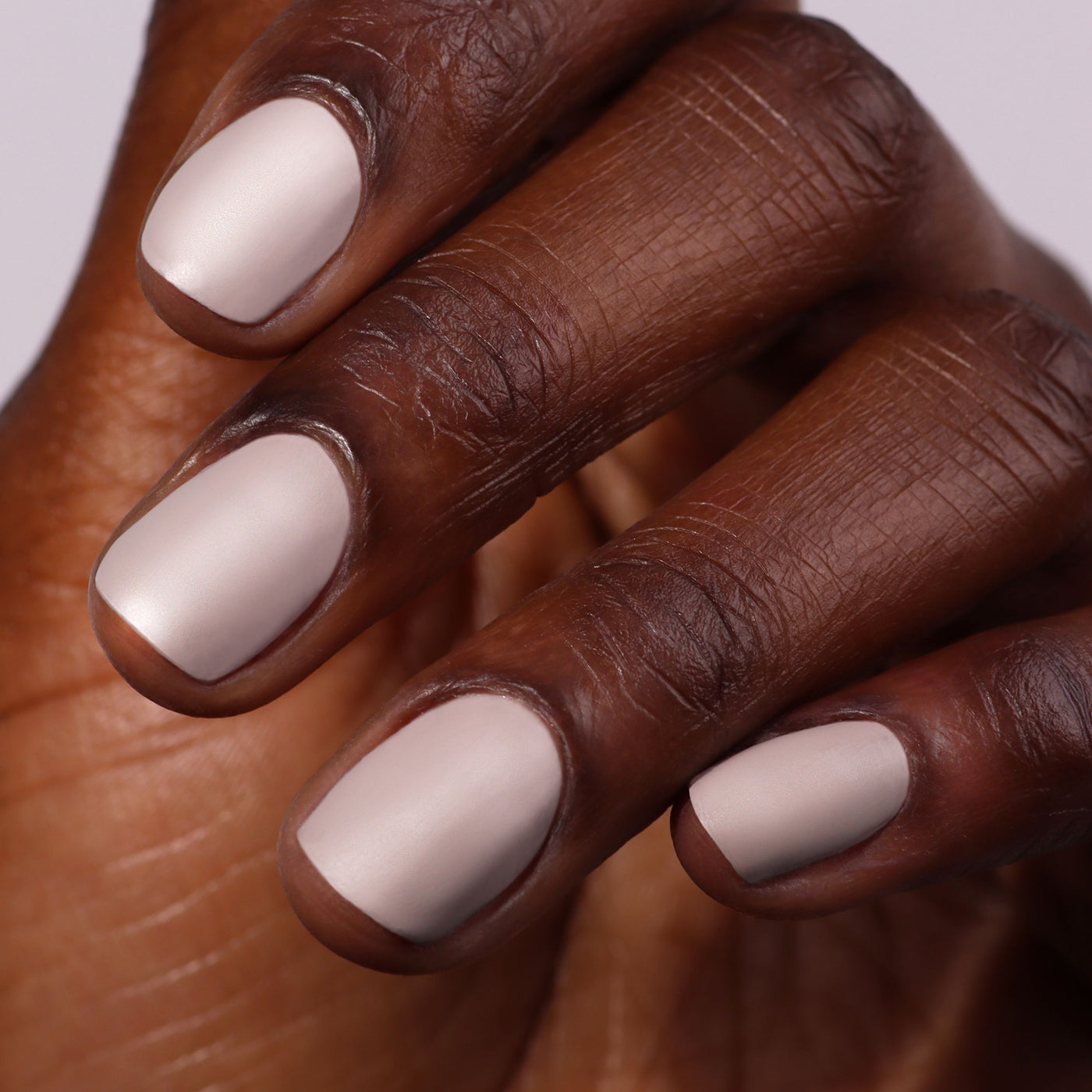 Close-up of a hand with neatly manicured nails painted in Beaumont, a light matte greige from LONDONTOWN's vegan, cruelty-free polish.