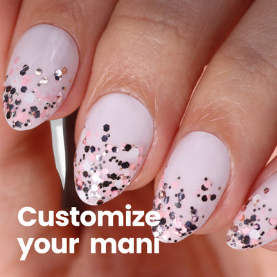 Close-up of manicured nails with LONDONTOWN's Snowglobe Confetti Topper, adding pink and black glitter sparkle. Text reads, "Customize your mani for the perfect finish.