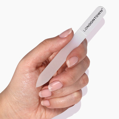 A hand holding a translucent LONDONTOWN Glass Nail File - Clear (Professional) promises effortless, damage-free nail filing.