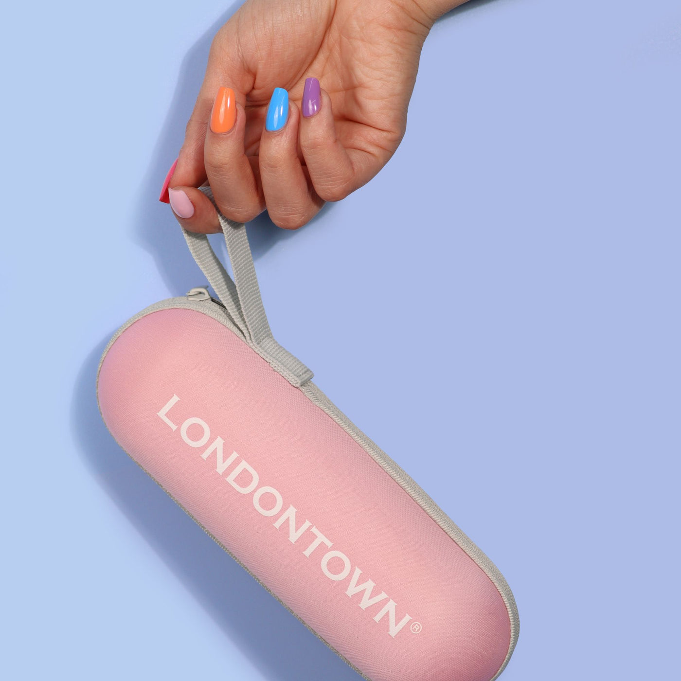 A hand with multicolored nails holds a pink Signature Mini Umbrella labeled "LONDONTOWN," a perfect travel companion against a light blue background.